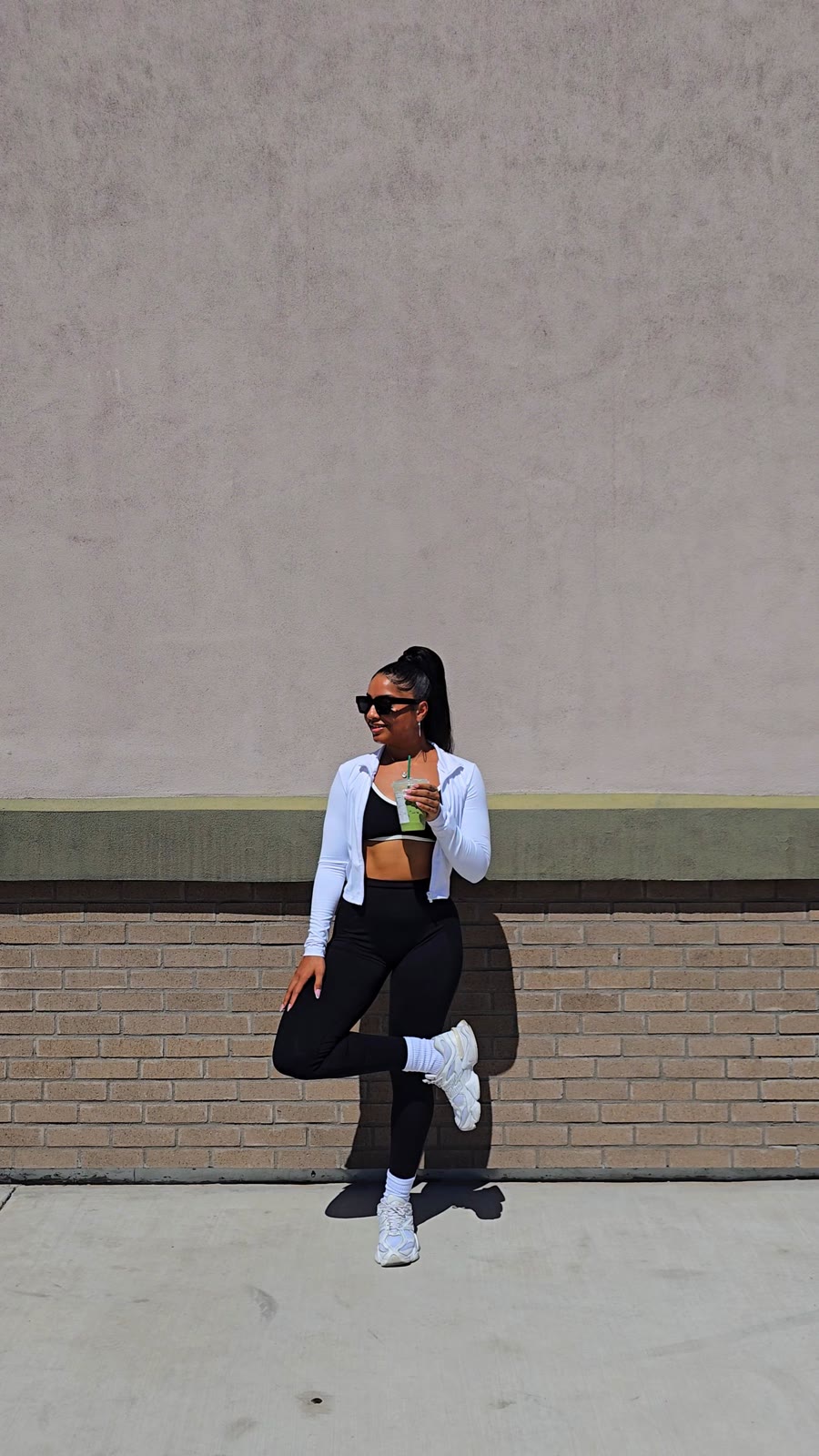 Layla in a white top and black pants, full-length, against a pale wall